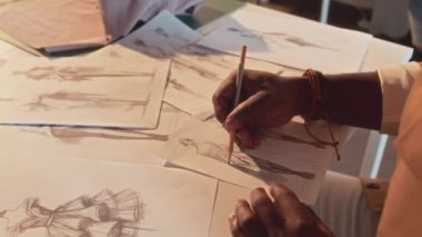 Tanımlanamayan kıyafet tasarımcısının yan tarafında atölyede oturan yeni moda kıyafetleri koleksiyonu çizimleri var.