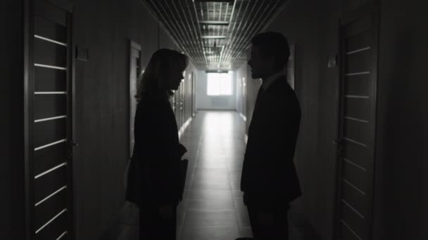 Обрезанный снимок в темном коридоре, где два неузнаваемых человека обсуждают свою работу в офисе и пожимают друг другу руки.