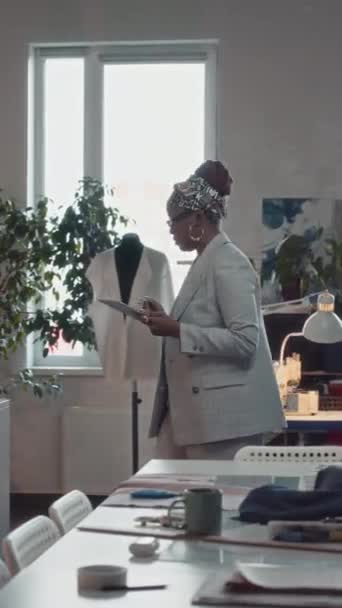 女性非洲裔美国人创意总监与平板电脑在控制服装制造过程的工作室中走来走去 — 图库视频影像