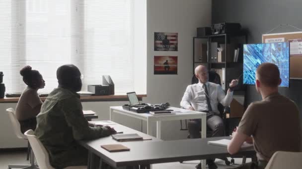 オフィスのスタッフミーティング中にスクリーン上の衛星マップを指す戦術戦略について軍将校に耳を傾ける認識できない軍隊士官の側面ショット — ストック動画