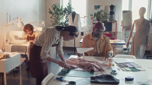 現代のカスタマイズスタジオで新しい衣料品コレクションを作成しながら アパレル生産プロセス中に多様な熟練したアトリエの労働者の側面ショット — ストック動画