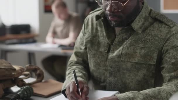 軍事アカデミーの授業中に勉強するメガネとカモフラージュのユニフォームを身に着けている黒人男性キャデットのキルトクローズアップ — ストック動画