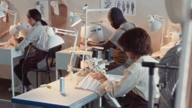 Önlüklü, endüstriyel giysi makinesiyle dikiş atölyesinde çalışan çeşitli terzilerden oluşan bir grup yan çekim.