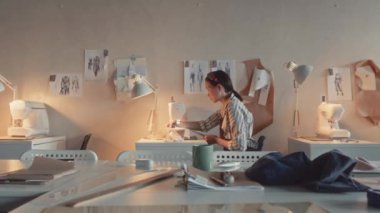 Endüstriyel giysi makinesiyle terzilik ya da tekstil terziliği yapan genç terzinin fotoğrafının yakınlaştırılması ve dikiş fabrikasından geçen kadın çalışanın görüntüsü.