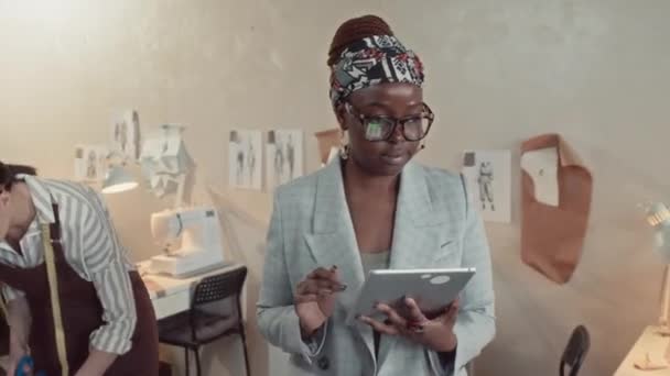 上班时间 带着眼镜和平板电脑走来走去 控制工作流程的时髦的非洲裔美国人裁缝店店主的示意图 — 图库视频影像