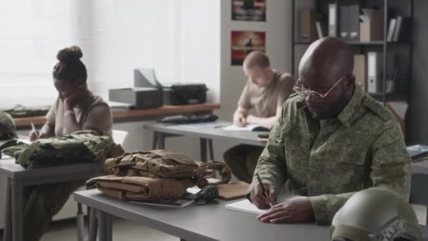 軍事アカデミーのトレーニングクラス中にメガネとカモフラージュのユニフォームライティングで男性のアフリカ系アメリカ人のキャデットのサイドショット — ストック動画