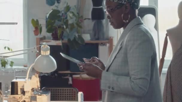 裁缝店的黑人女业主在服装制造机上经过一组不同的服装制造商的倾斜制片镜头 — 图库视频影像