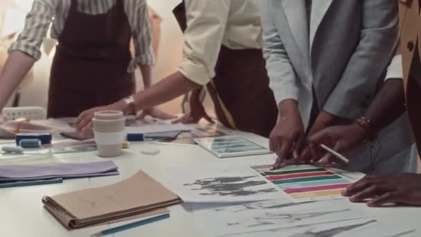 アトリエの労働者の多様なチームのティルトサイドショットは テーリングスタジオでのワークデー中にスケッチ ファブリック カラーパレットを使用して新しいファッションコレクションを製造するプロセスを議論します — ストック動画