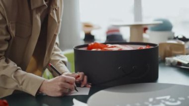 Doğum günü dileklerini hediye kartına yazıp hediye kutusuna koyan tanınmamış kadın tasarımcının orta boy yakın çekimi.