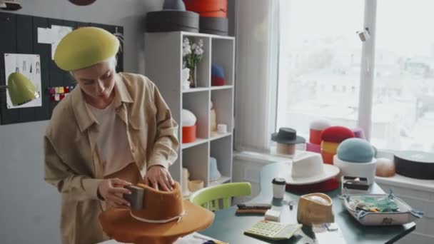 新しい帽子を磨くスタジオに立っている若い白人女性の中型ショット — ストック動画