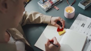 Kadın tasarımcının, atölyesinde otururken yeni şapka versiyonlarını çizdiği omuz üstünden.