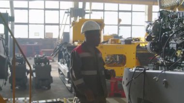 Tulumlu siyah fabrika işçisinin makine fabrikasında traktör iç patlama motoru teşhisi koyarken yan görüntüsü.