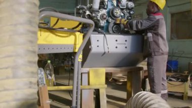 Siyah erkek fabrika işçisinin sarı kasketli tam eğim ve makina fabrikasındaki traktör iç yanmalı motorda esnek elementler ve makara tamiri