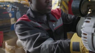 Sarı şapkalı ve üniformalı Afrikalı Amerikalı erkek işçinin yakın çekimi. Tesiste traktörün içten yanmalı motorunun elementlerini tamir ediyor.