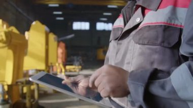 Fabrikadaki makine üretim sürecini incelerken, tablet üzerinde veri yazan Kara Fabrika denetleyicisinin yan eğik görüntüsü