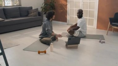 Irklar arası çiftin yere oturup yoga videosu izlediği ve tekrar ettiği görüntüyü yakınlaştır.