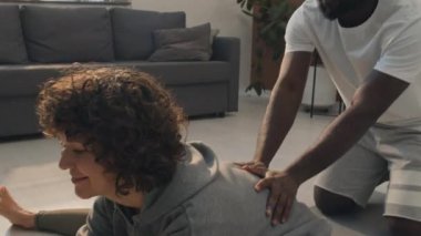 İyi ışıklandırılmış bir odada erkek arkadaşının yardımıyla egzersiz yapan mutlu bir kadının orta pozu.