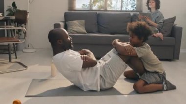 Oğlunun bacaklarıyla mekik çekerken ve karısının dijital tabletle kanepede otururken.