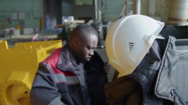 Siyah fabrika işçilerinin yavaş yavaş üniformalarını giyip, beyaz şapka takıp fabrikaya gitmeleri.