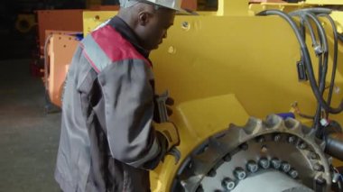 Siyahi erkek fabrika işçisinin vidaları ya da fındıkları vidaları vidalarken ve yorgun bir şekilde dönerken görüntüsü makine fabrikasındaki alın terini siliyor.