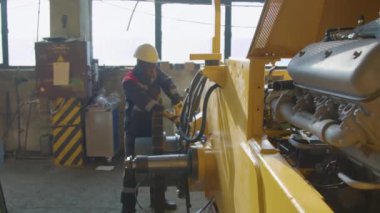 Kara şapkalı fabrika işçisinin yakınlaştırılmış görüntüsü. Vites tekerindeki vidaları sıkıyor. Makine fabrikasındaki traktör çerçevesinde.