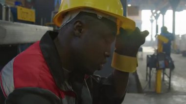 Yorgun siyahi işçilerin sıkı çalıştıktan sonra dinlenirken, kaskını çıkarırken ve makine fabrikasında alnından ter silerken göğsünden çekilen bir kare.