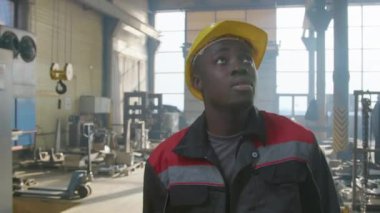 Sarı başlıklı ve kamuflajlı Afro-Amerikan fabrika işçisinin, fabrika hattı üretimini denetlerken çekilen görüntülerini takip edin.