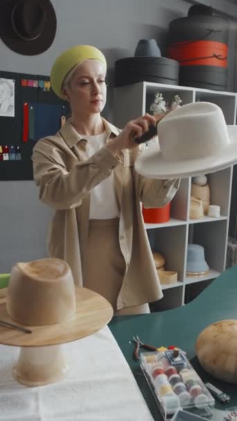 Вертикальный Снимок Молодого Шляпника Стоящего Мастерской Чистит Новую Белую Шляпу — стоковое видео