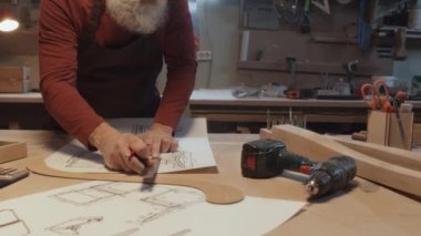 Tanımlanamayan marangozun gri sakallı, yeni inşaat çiziminde sandalye hatlarını ölçen görüntüsü.