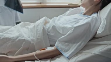 Doktor, kadın hastasının röntgen taramasından sonra yatakta yattığını gösteriyor.