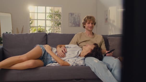 年轻女子的男朋友们在电视上看电影时 一头乌黑的卷曲的头发躺在他们的腿上 — 图库视频影像