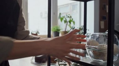 Seçici odak noktası tanınmayan kadın baristanın elleriydi. Kahve dükkanındaki raflara cam kavanozlar ve kurabiyeler koyardı.