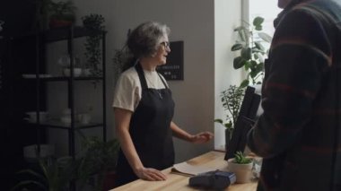 İki kadın kahve dükkanı çalışanı siparişini hazırlarken, erkek müşterinin dışarıdan yemek alıp parasını ödediği orta boy bir fotoğraf.