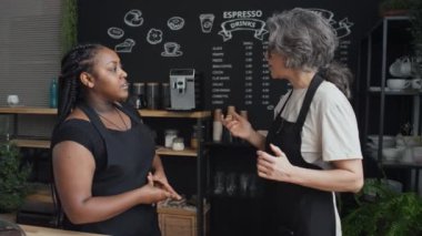 Kafkas kafeterya işçisinin yeni siyahi kadın baristaya zevkle danışmanlık yaptığı orta boy bir fotoğraf.