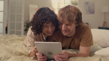 Genç bir adamla kadının, iyi ışıklandırılmış bir odada, dijital tablet kullanarak internete baktıkları orta ölçekli bir fotoğraf.