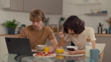 İki genç insanın kahvaltı yaparken teknolojilerini kullandıkları orta boy bir fotoğraf.