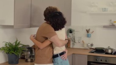 Genç çift, düzenli mutfaklarında dururken sohbet ediyor ve sarılıyorlar.