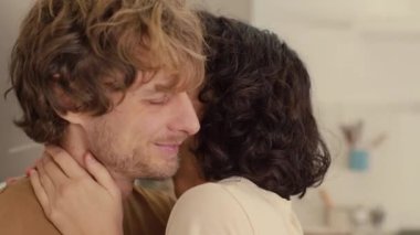 Genç çiftin, mutfaklarında birbirlerini öperken sarılıp kucakladıkları orta ölçekli bir fotoğraf.