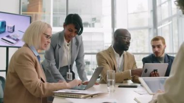 Resmi gri takım elbiseli genç bayan şirket çalışanı toplantı sırasında laptopunu kullanarak iş arkadaşıyla konuşuyor.