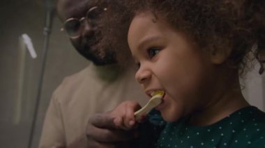 Babası ona rehberlik ederken diş fırçasıyla diş fırçası kullanan kıvırcık saçlı küçük kıza odaklan.