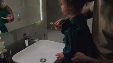 Babası banyoda durmuş diş fırçası ve diş macunu kullanarak kızına diş fırçalama sürecinde rehberlik ediyor.