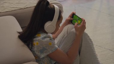 Kanepenin yanında oturan modern kızın akıllı telefonuyla online oyunu kazandıktan sonra mutlu olduğu yüksek açılı bir fotoğraf.