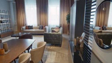 Tarafsız gölgeli oturma odasının iç tasarımı ahşap yemek masası, renkli yastıklı gri kanepe ve büyük yuvarlak siyah ayna.