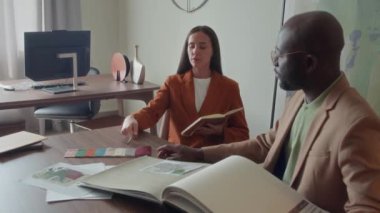İş yerinde oturan kendine güvenen mobilya danışmanı müşterisine evi için doğru paleti seçmesinde yardım ediyor.