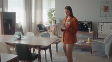 Mobilya mağazasında portre yöneticisi portresi, turuncu ceket giyiyor, oturma odasının modelinin ortasında duruyor, kameraya bakıyor.