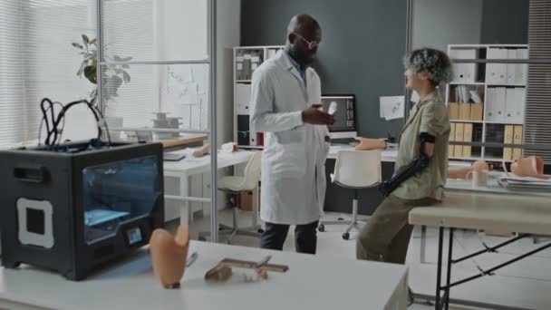障害のある患者と話す3D印刷機で医学研究室に立っている黒人の監督医 — ストック動画