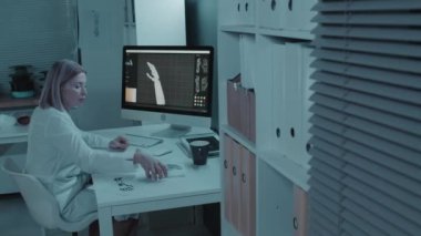 Beyaz, orta yaşlı bir kadın monitörün arkasında oturmuş protez kolun yeni 3D modelini geliştiriyor.