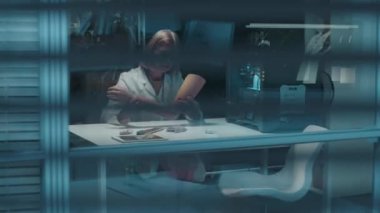 Masaüstünde oturan kadın mühendisin perdelerine bakın. 3D yazıcıyı izlerken yeni protez üzerinde çalışıyor.