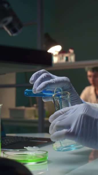 无法辨认的女科学家将蓝色液体倒入瓶中 加入绿色底物 然后将内容混合在一起 检查结果 — 图库视频影像
