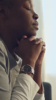 Tıbbi üniformalı, yorgun, genç, siyah bir kadının iş arasında ya da evde otururken, ağrıyı ya da kas spazmını azaltmak için boynuna kapalı bir şekilde masaj yaptığı dikey bir fotoğraf.